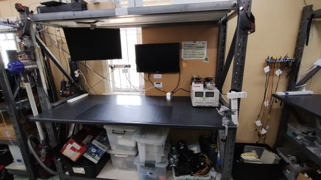 Workbench bay with monitors, bench power supply and storage tubs in the Workshop